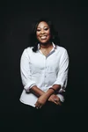 A photo of a woman in a white button-down shirt with her arms crossed smiling