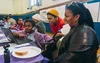 A woman looks at a laptop that is sitting at a table while two young children gather around to look at the laptop as well. Everyone is smiling.