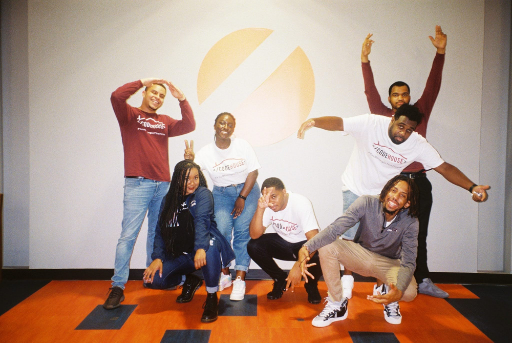 A group of people stand together on an orange rug.