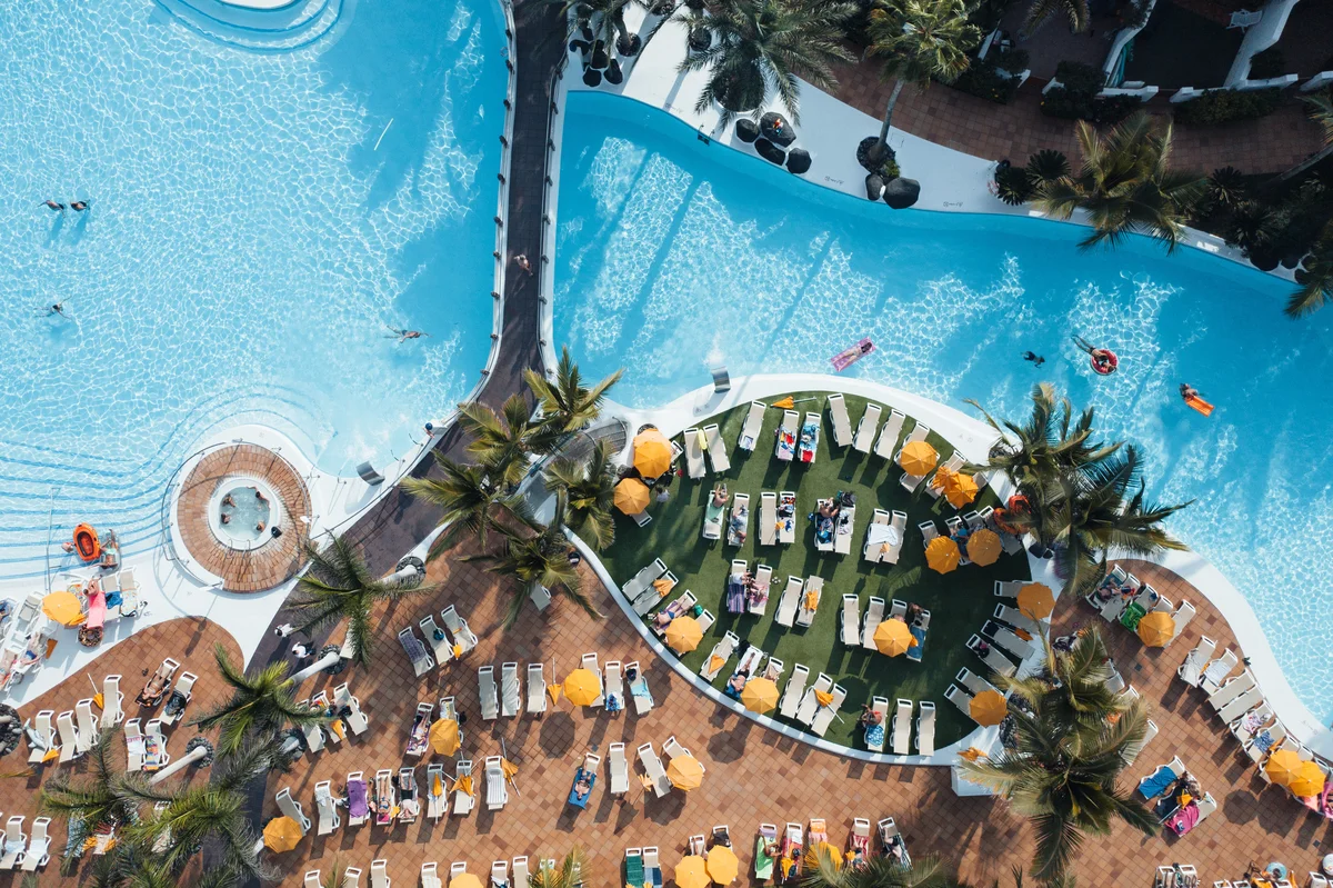 Top-view image of vacation resort with a pool, trees, and lawn chairs.