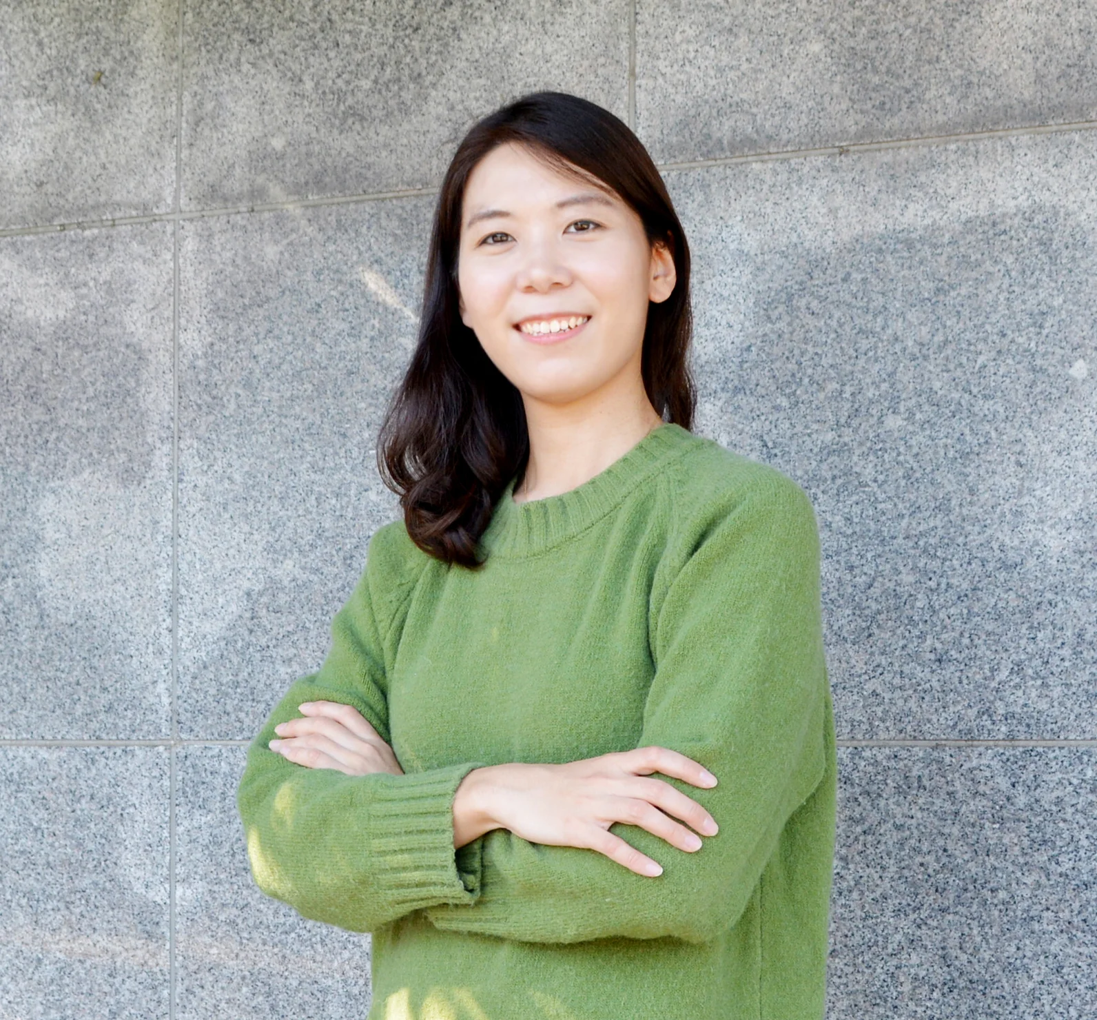 A person smiles and stands in front of a wall with her arms crossed.