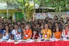 A group of people seated at a long table, with children standing behind them, making a heart sign with their fingers