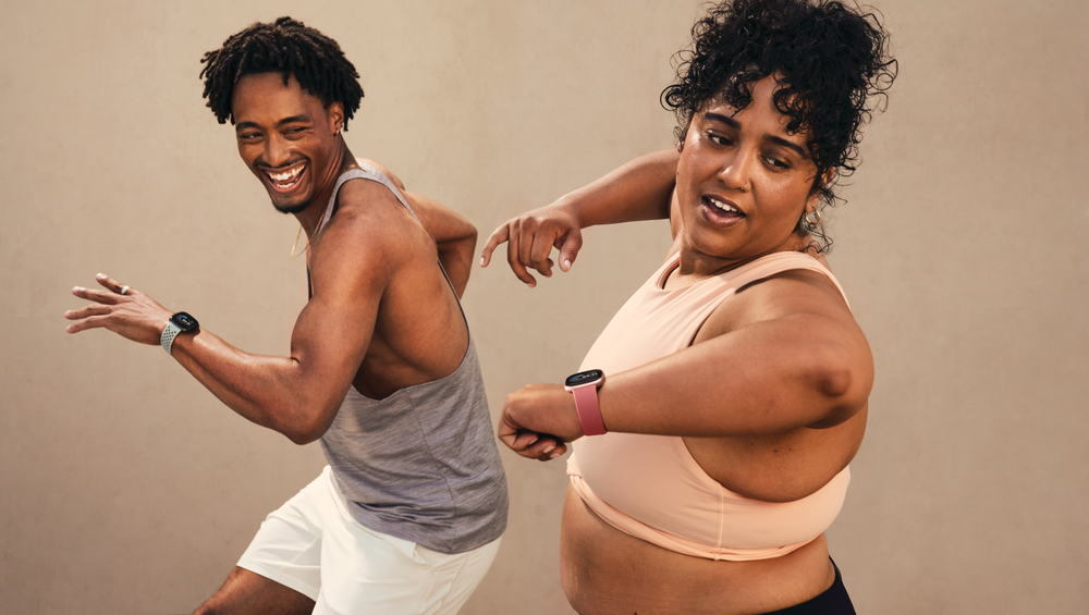 A man and woman exercise with Versa 4 on their wrists.