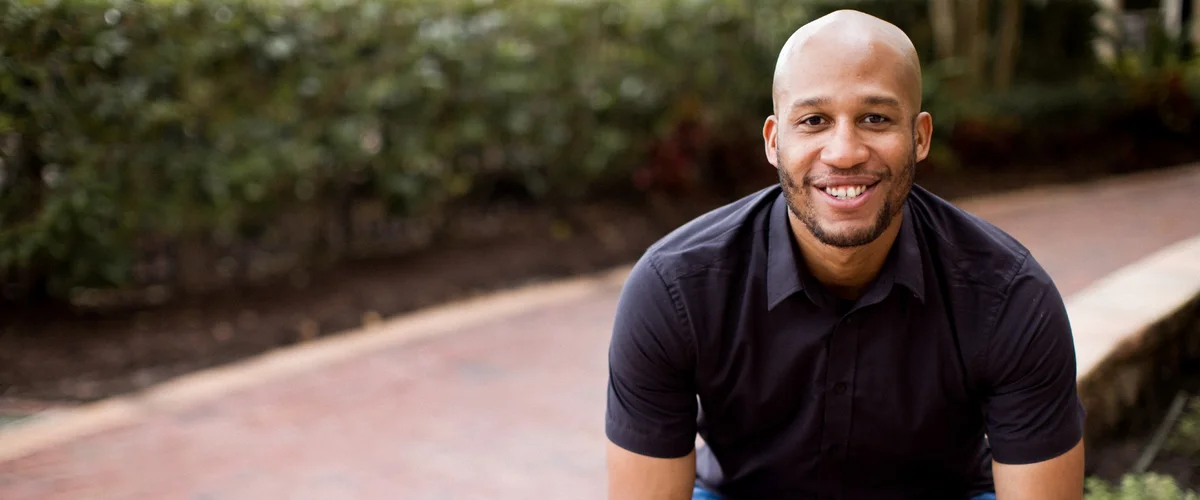 Rich Jones, wearing a short-sleeved collared shirt, sitting outside smiling at the camera.