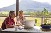 a woman and a man are looking at a laptop, behind them is an Australian scenery