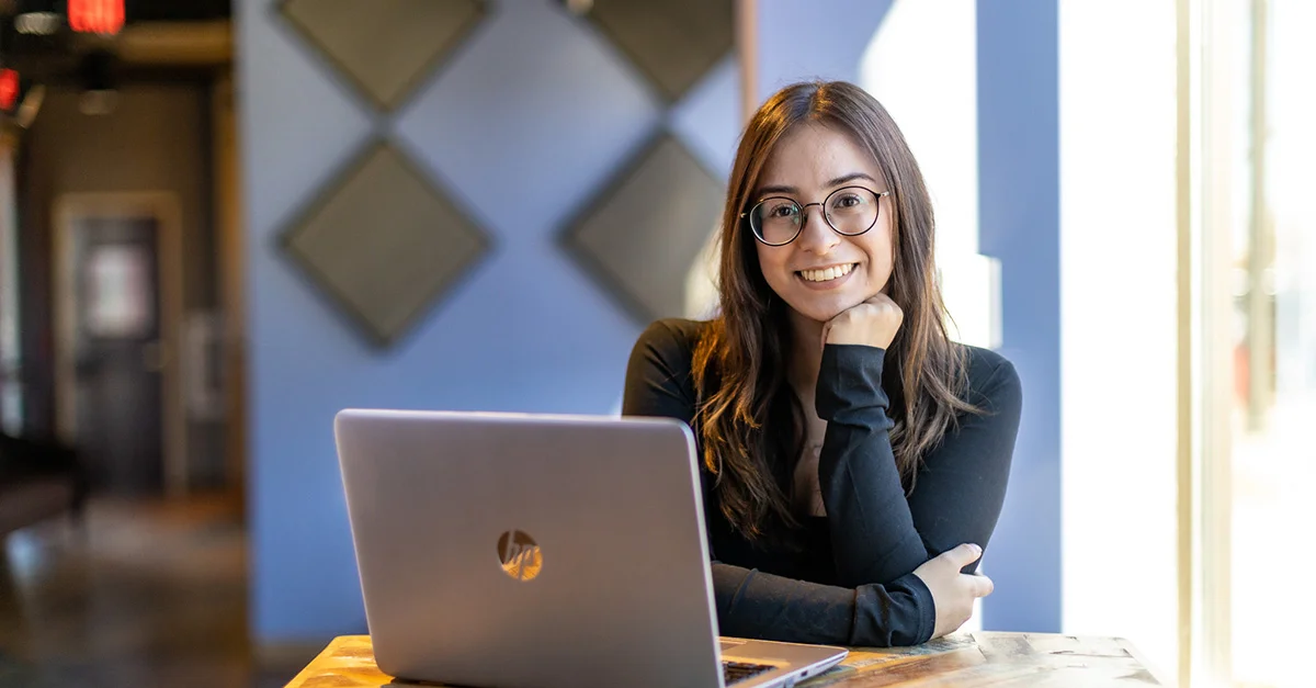 A woman with brown hair sits at a desk using a laptop