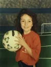 Mackenzie as a young girl wearing a red T-shirt and holding a soccer ball.