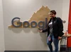 Joy stands in front of a Google logo across a piece of wood cut in the shape of Virginia.
