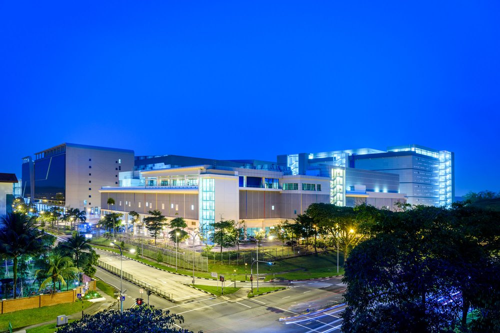 Large data center building illuminated by blue and yellow lights against a dark royal blue sky. In the foreground are palm trees, grass and city streets.