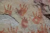 A rock wall with four handprints in red, along with additional partial handprints in view