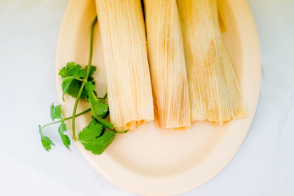 Three tamales and a sprig of cilantro sit on a pale, off-white plate.