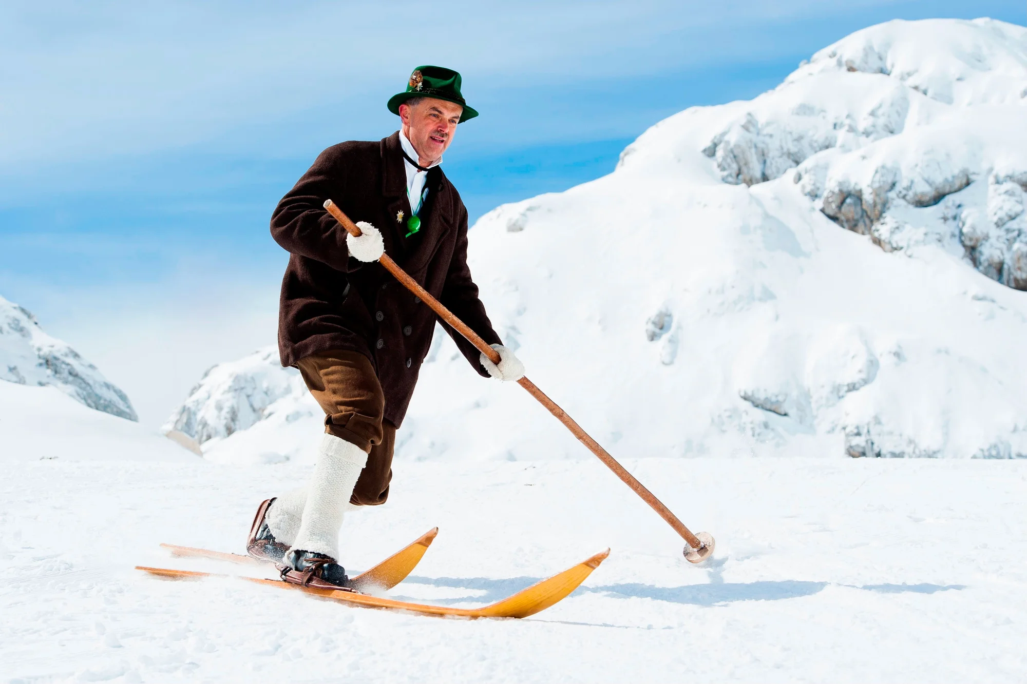 A picture of a man skiing in the snow with vintage skis and holding one large wooden pole