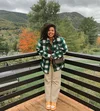 Tyla-Lauren stands on a deck outside with a checkered flannel shirt. A mountain and trees with changing color leaves are in the background.