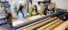 Two women standing over a large drafting table. They are smiling at one another and appear to be discussing something. There is a graphic print on the table they are looking at.