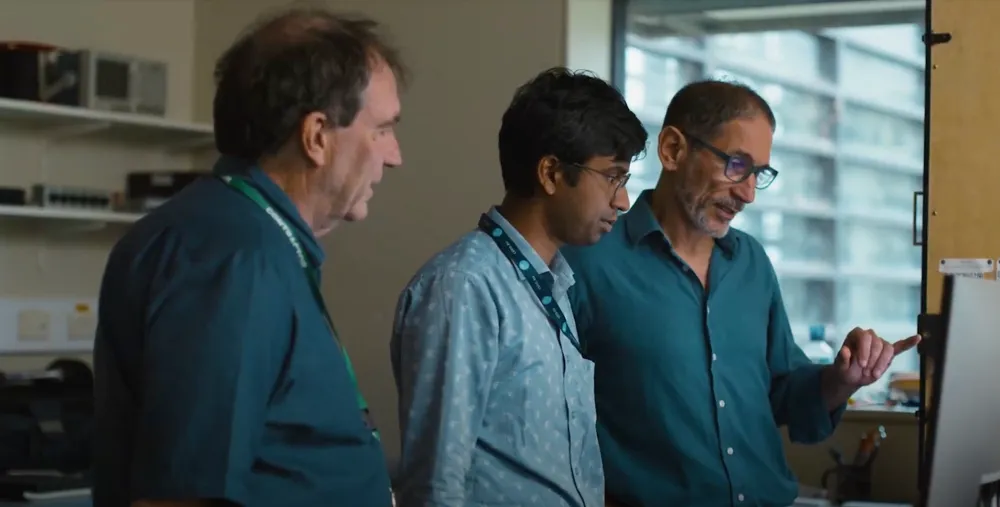 A video thumbnail of three male scientists standing and talking around a computer