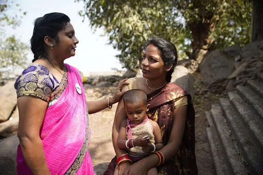 A photo showing two women in traditional dress in rural India, one of them holding a baby.