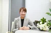 a photo of Mom Sitter founder Jeeyea Chung in a business suit, sitting at an office table next to some white flowers
