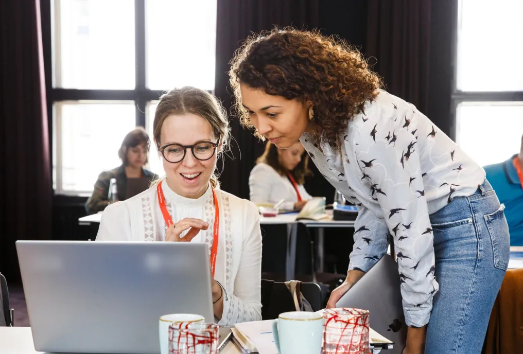 A photo of two people working and looking at a laptop