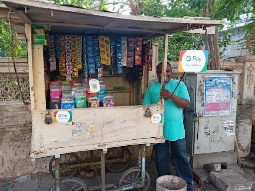 A merchant standing next to a stall on the side of the road in India, with signs indicating that he accepts Google Pay as a payment method.