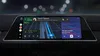 A digital dashboard display shows the Android Auto interface. There are circular app icons on the left and a map in dark mode taking up the bulk of the display, with a text at the top from Jayson Jackson that says let’s grab coffee before the meetingA pink and purple square on the right of the display shows a song playing, with the song title You got to listen by artist Michael Evans.