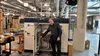 A photograph of Dr. Leo Casey smiling and standing in front of a traditional inverter in Tapestry’s labs in Mountain View.