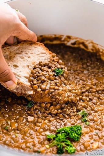 A hand dips a piece of bread into a pot of lentil soup.