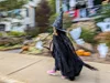 A photo of a child wearing a witch costume while walking down the sidewalk. The houses in the background are blurry, indicating the subject is in motion, while the subject remains sharp.