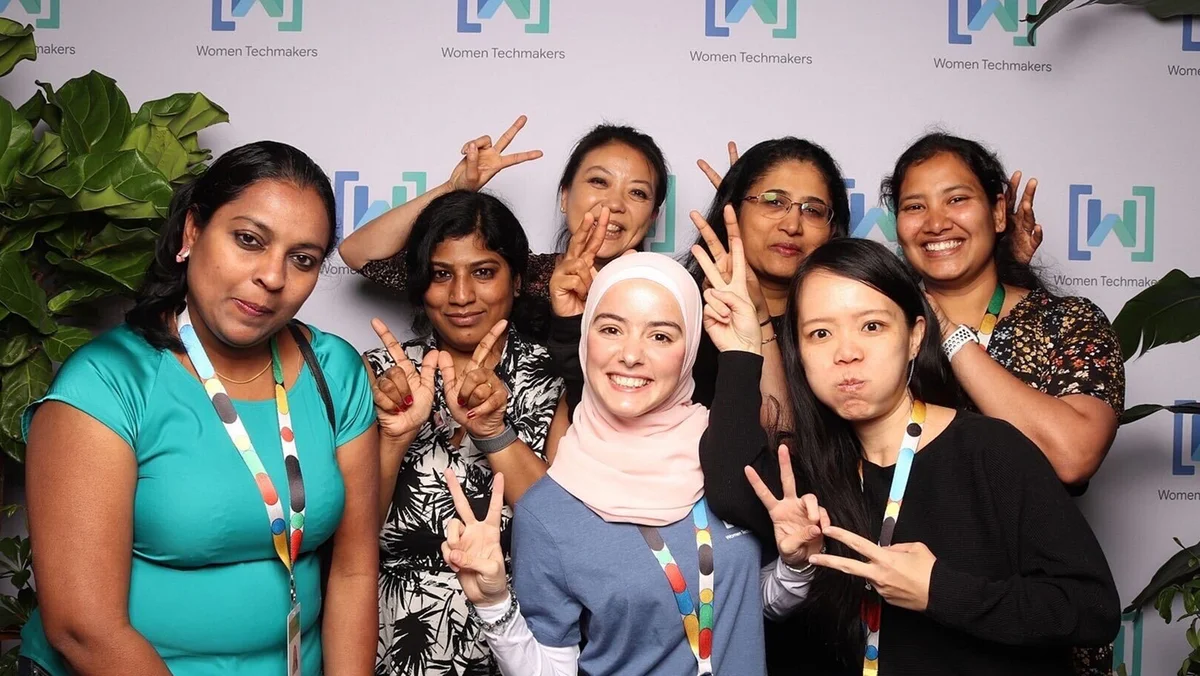 A group of women in front of a Women Techmakers backdrop smiling at the camera. Alaa, wearing a headscarf, is in the center.