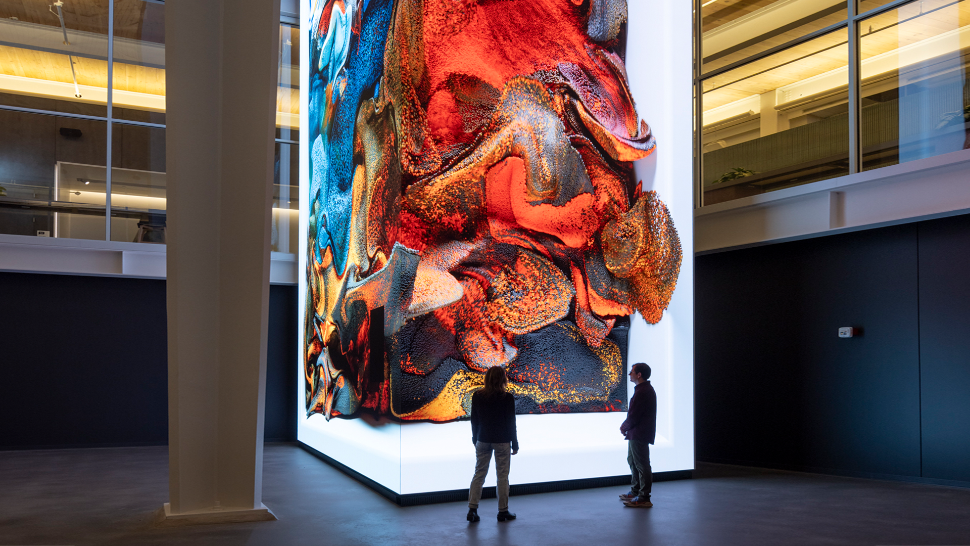 Two people viewing a colorful, floor-to-ceiling abstract digital installation.