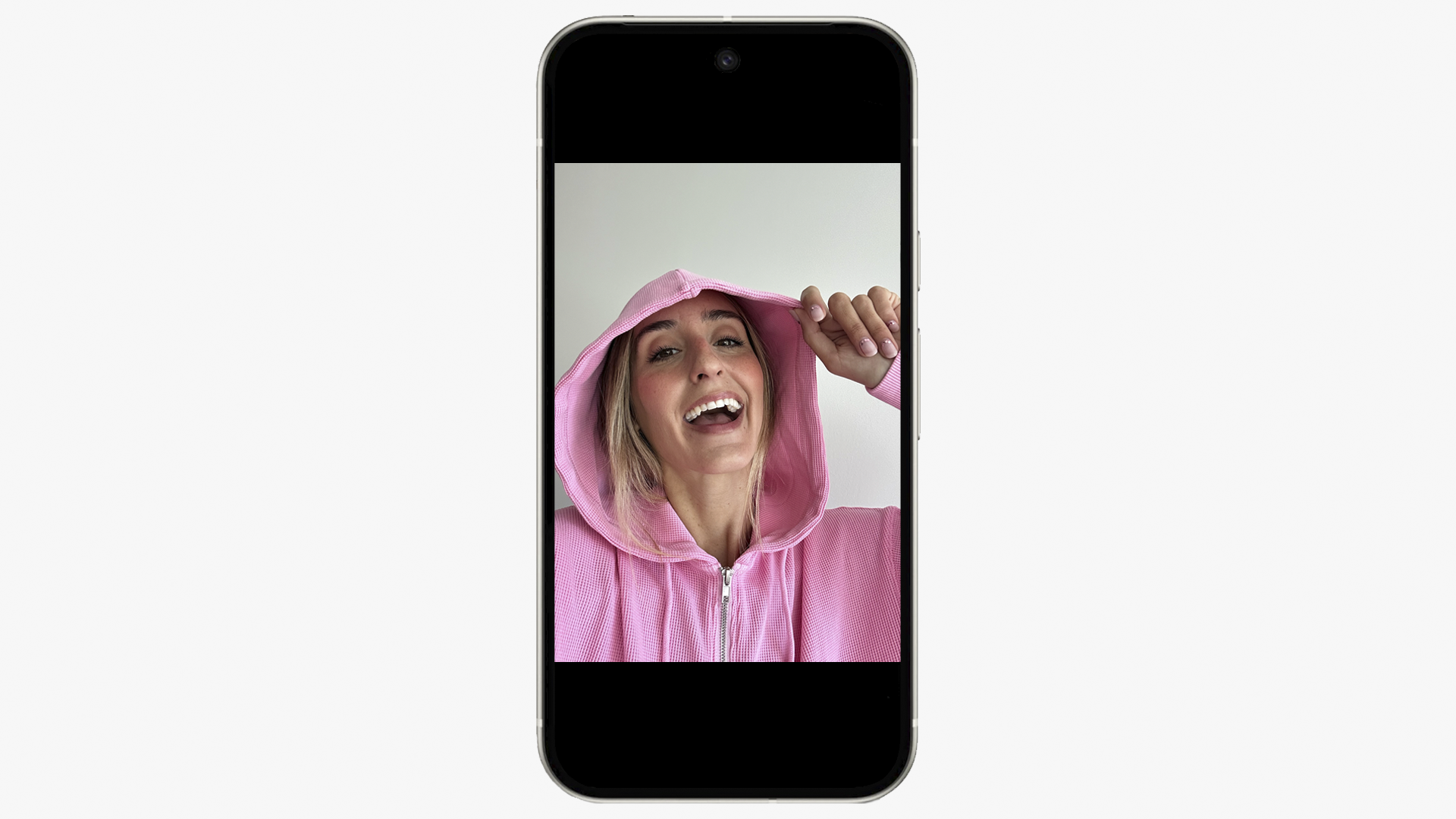 A smartphone displays a close-up photo of a smiling blonde woman wearing a pink zippered hoodie and holding the hood over her head.
