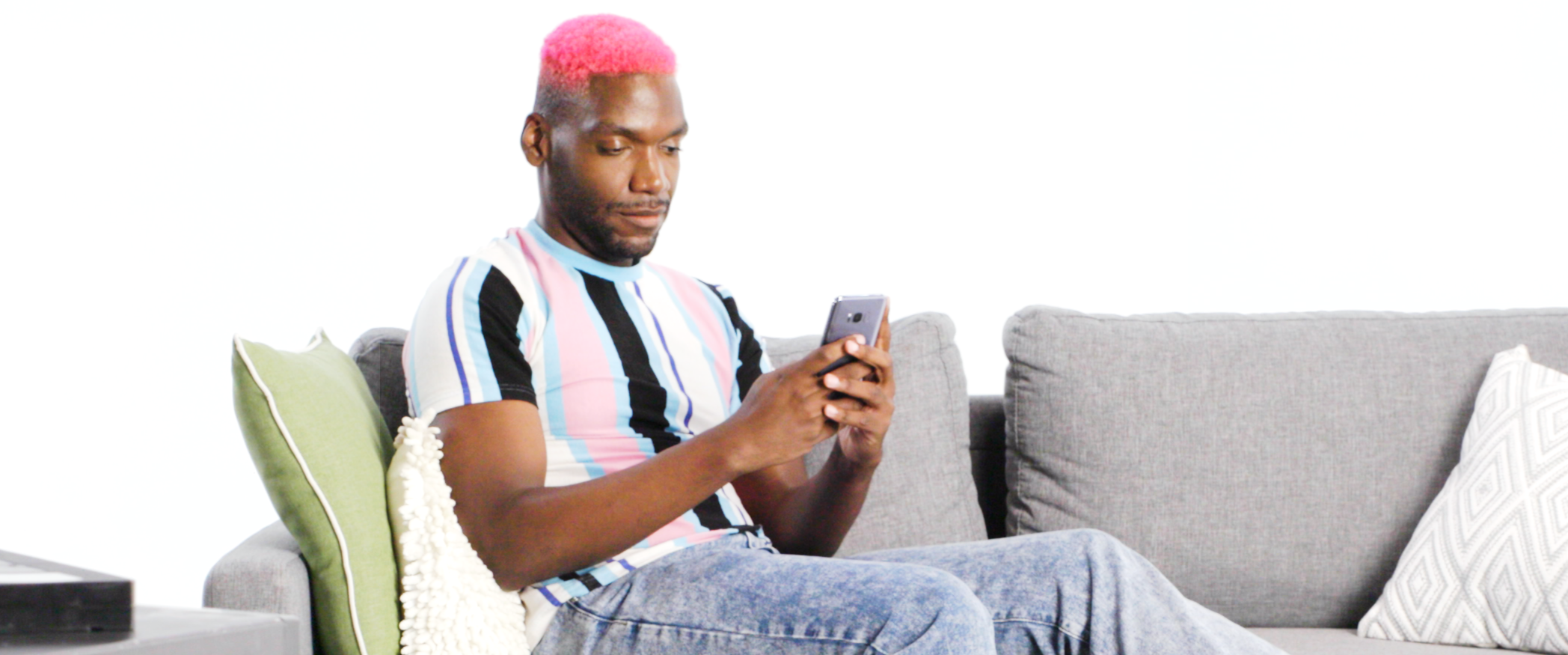 A man wearing a striped shirt is sitting on a couch looking at his smartphone.