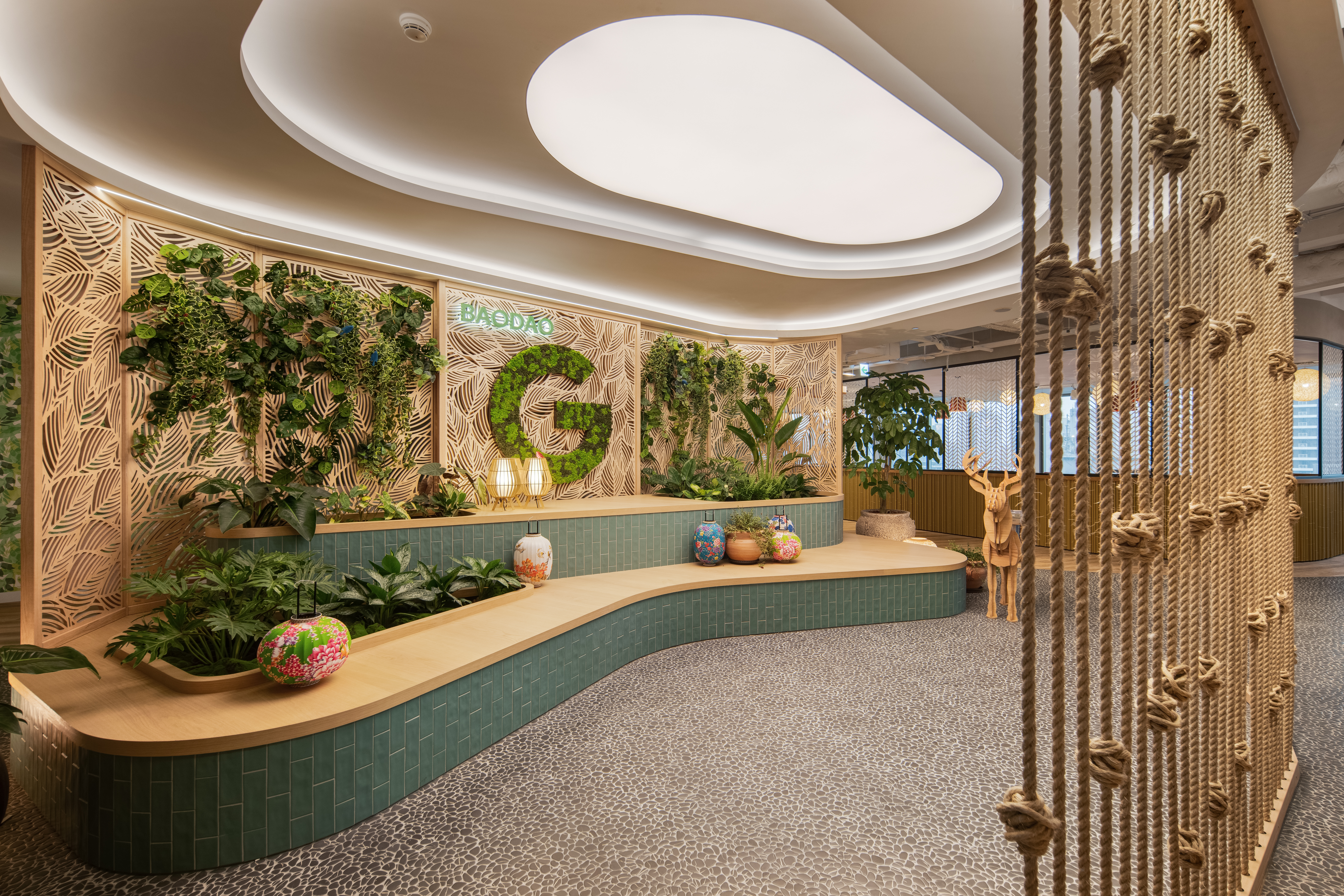 Photo of a room with a soft curved shelf, plants, and a large “G” logo on a wooden wall