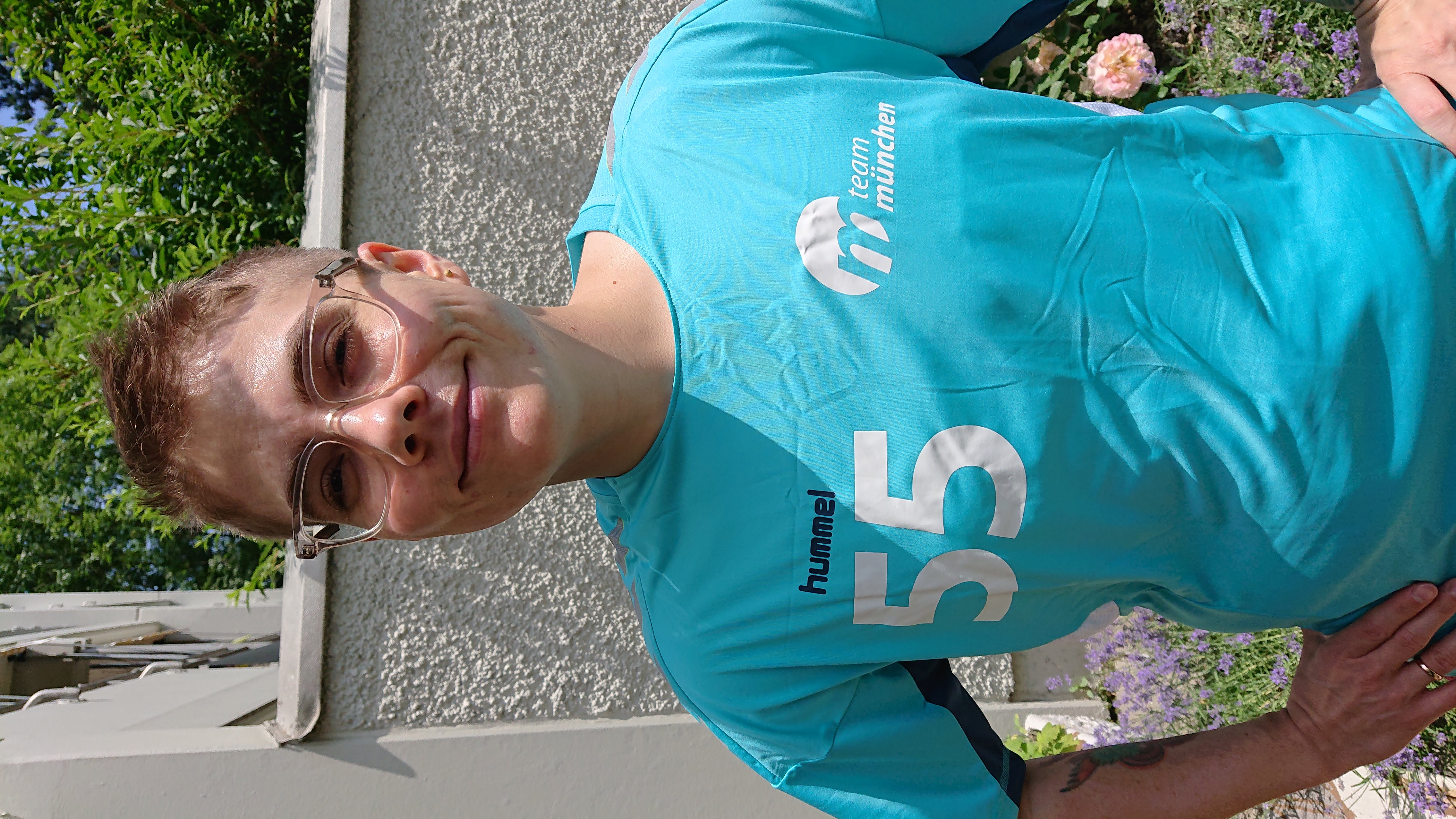 Adrian Hausner steht vor einer Mauer und trägt ein T-Shirt der Handballmannschaft von Team München