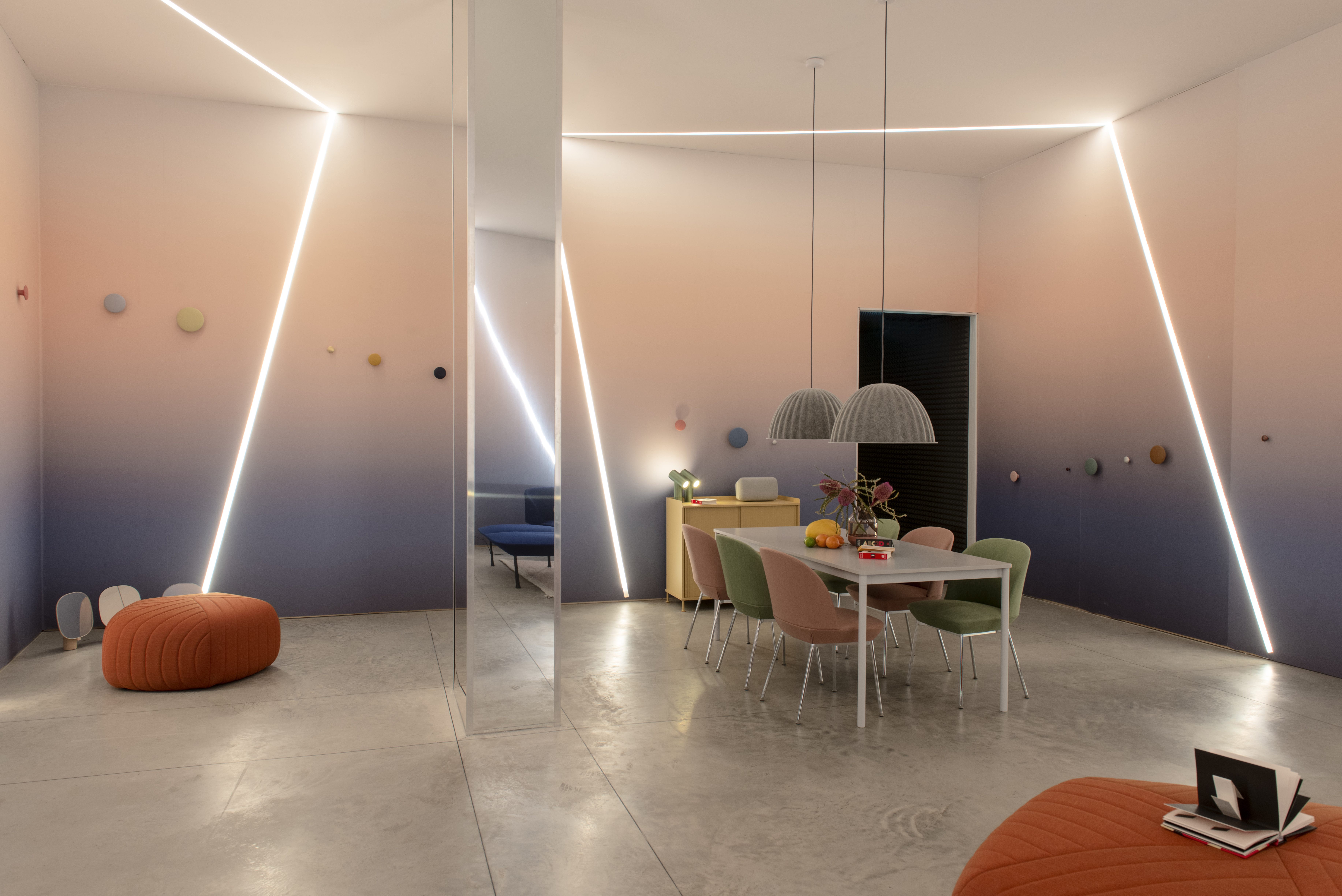 A room with diagonal lights across the walls and a table with green and pink chairs.