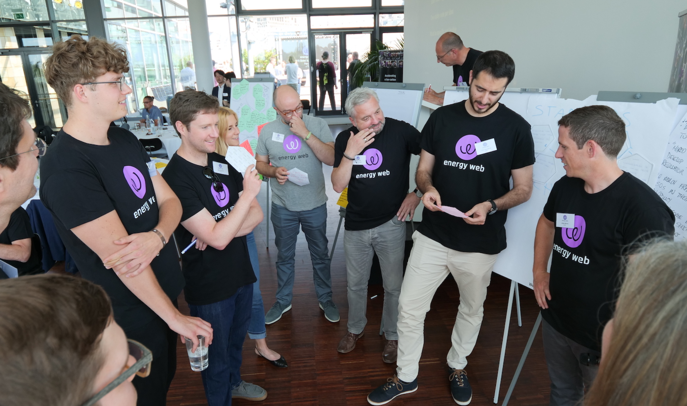 A group of people in Energy Web Foundation shirts huddled together in an office.