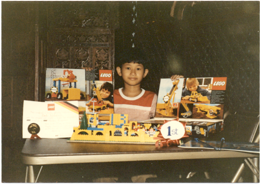 Paolo standing with two Lego boxes on either side of him. In front of him on the table is a fully constructed Lego set.