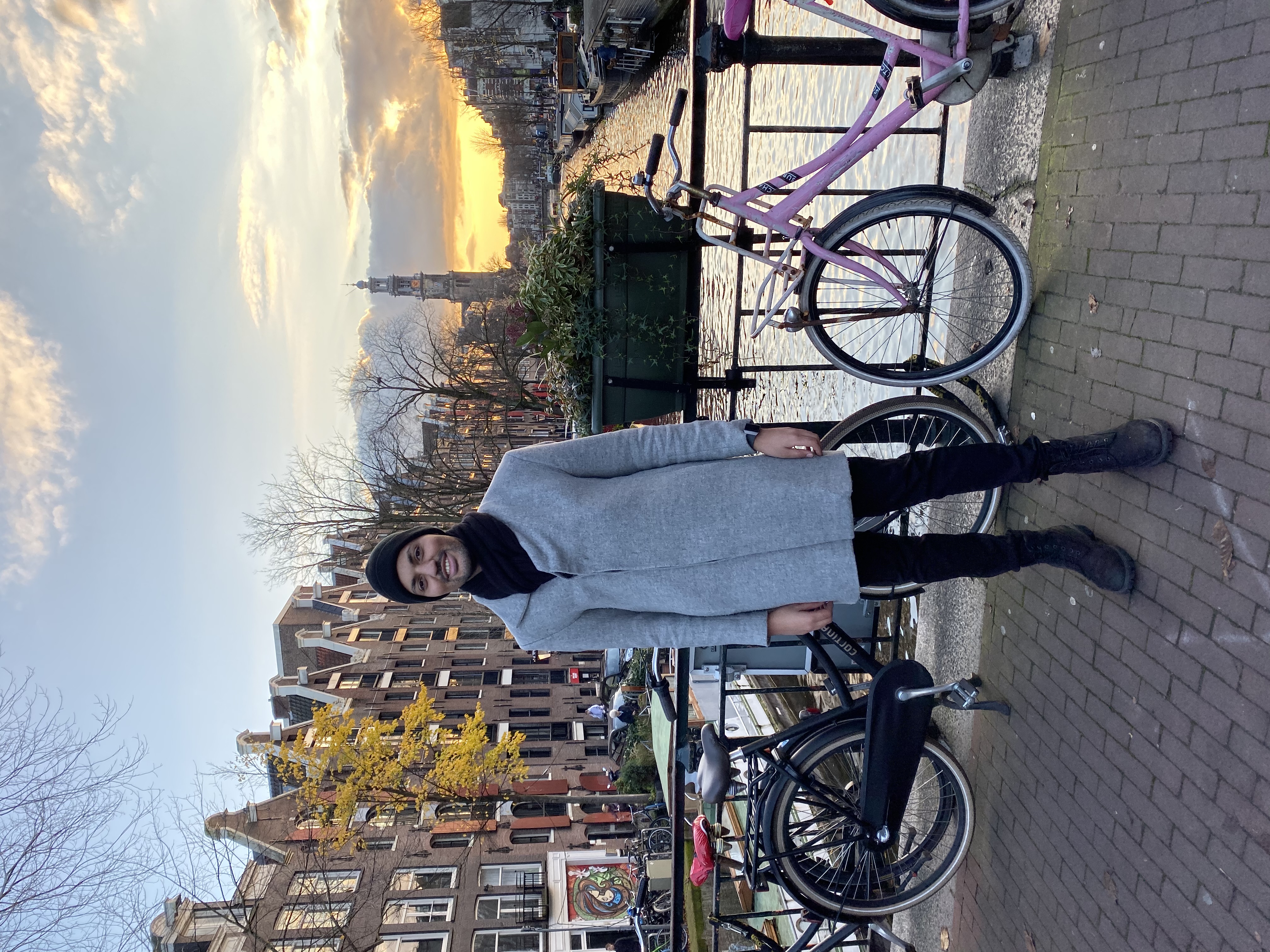 Bilal steht auf einer Grachtenbrücke in Amsterdam. Im Hintergrund der Sonnenuntergang.