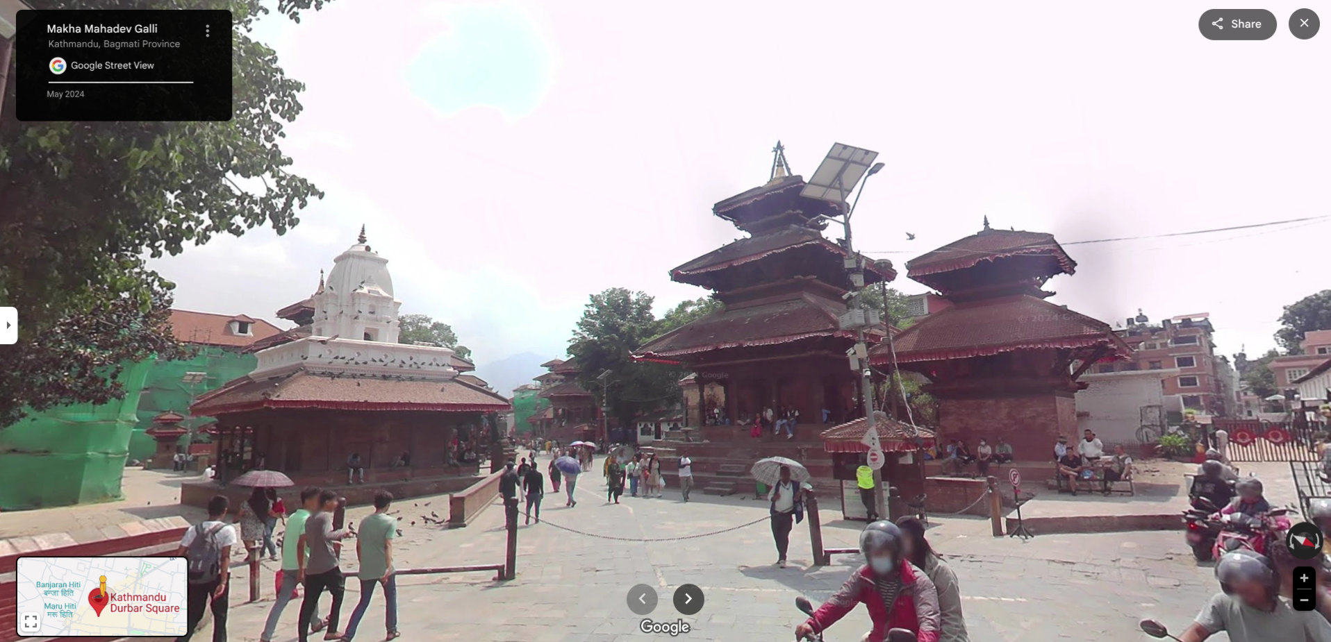 A street view of the historic Kathmandu Durbar Square, with people walking amongst traditional pagoda and white shikhara temples.