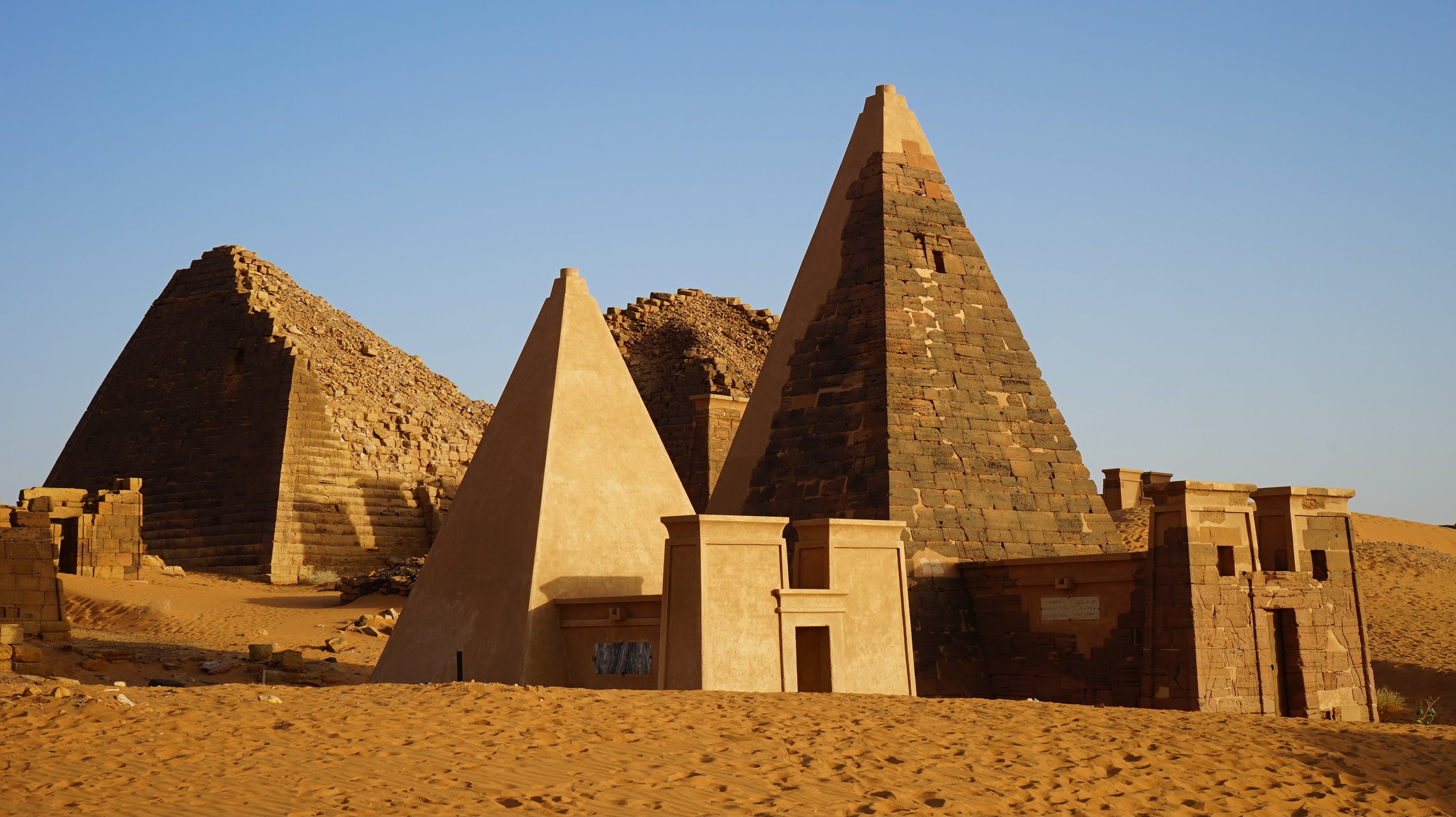 Two pyramids and their entrances with other pyramid remains in the background amidst the desert landscape.