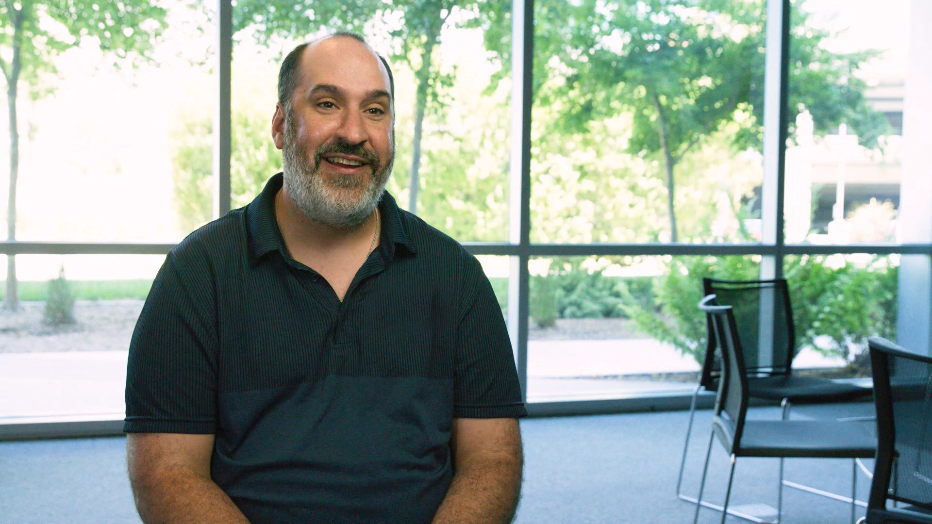 Image of a bearded man in a dark polo sitting and smiling.