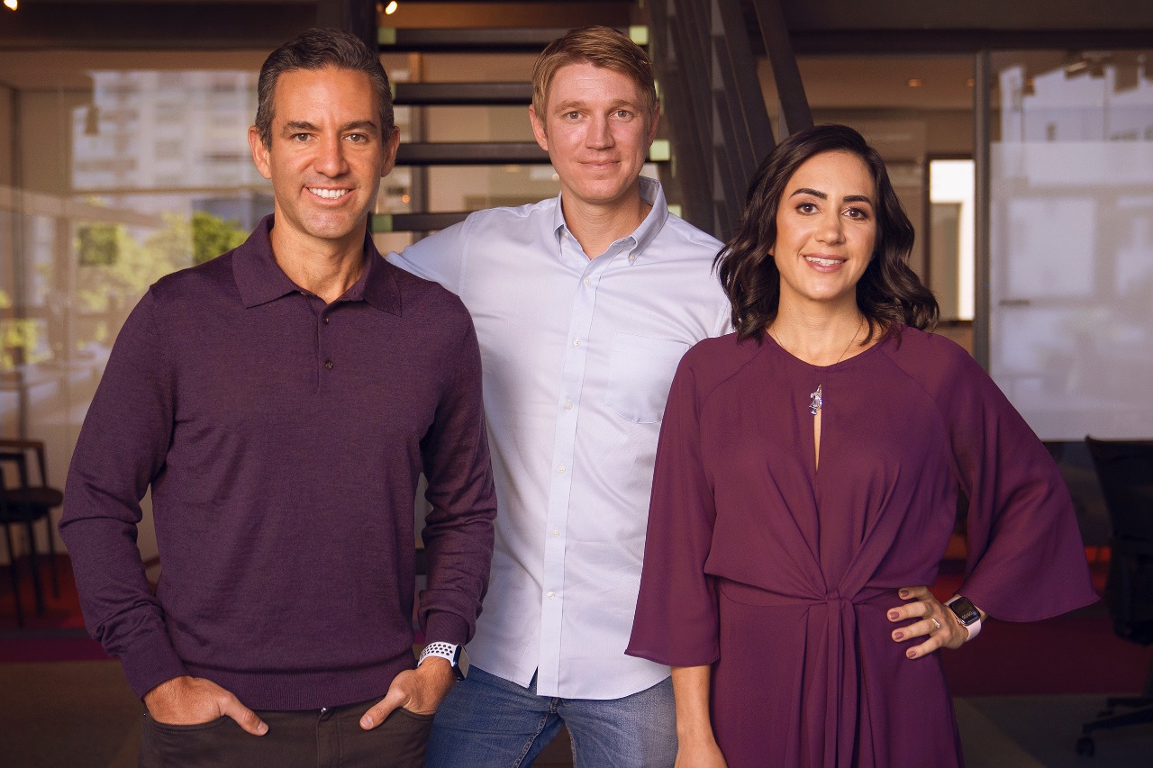 Two men and a woman stand facing the camera, smiling.