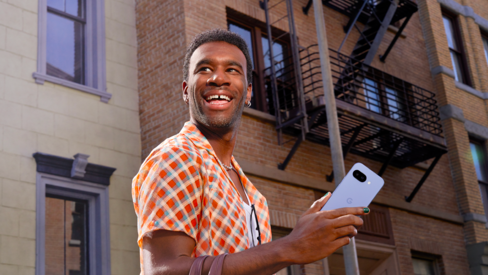 A young man is smiling and looking upwards to the left. He is holding a light purple smartphone in his hands.