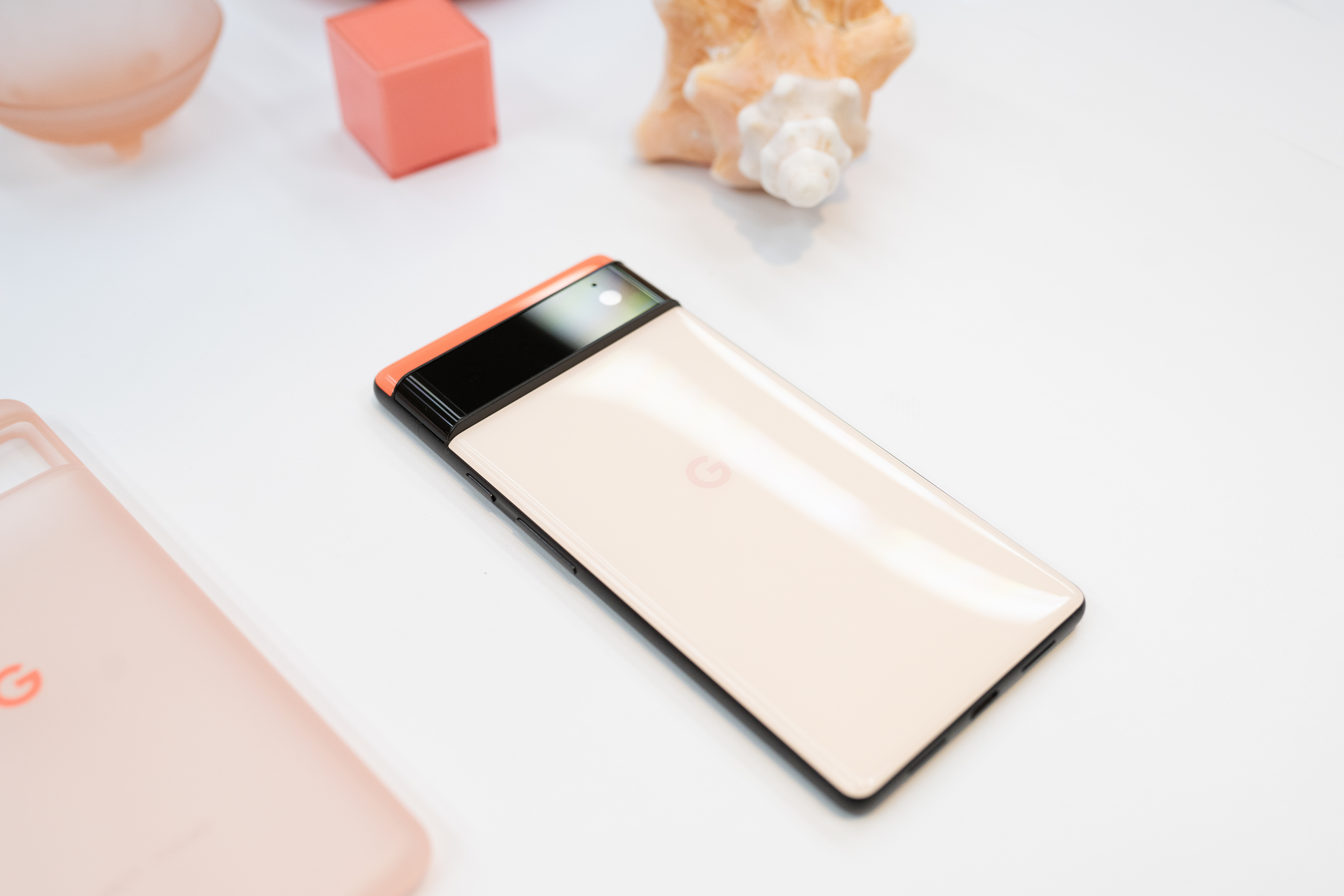 Photograph of the Kinda Coral Pixel 6 next to a pink cube and a pale pink shell.