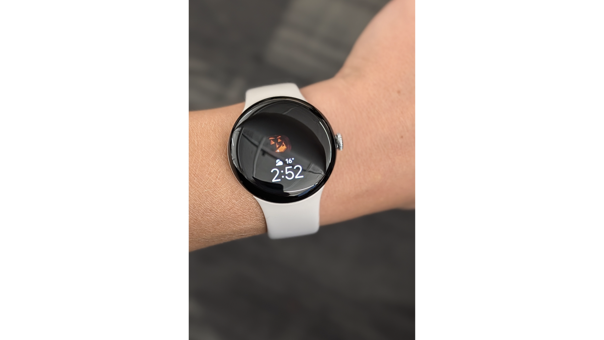 A Google Pixel Watch on a wrist, displaying a Halloween watch face with a jack-o'-lantern and the time 2:52.