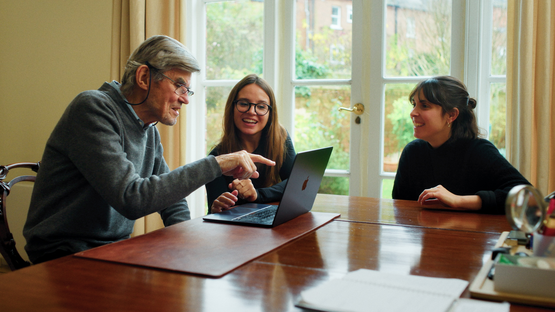 3 people sitting on a table and working together on a computer