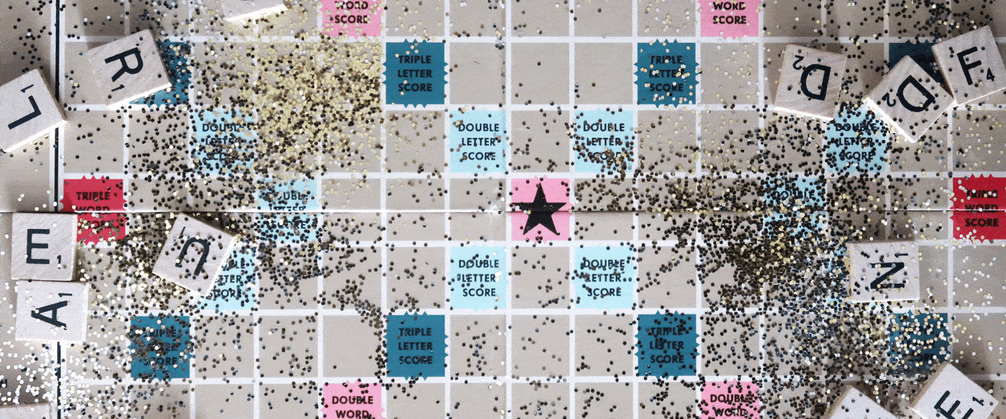 Animated GIF showing a Scrabble board with glitter and letters scattered on it. The words "Year in Review" are placed on the board.