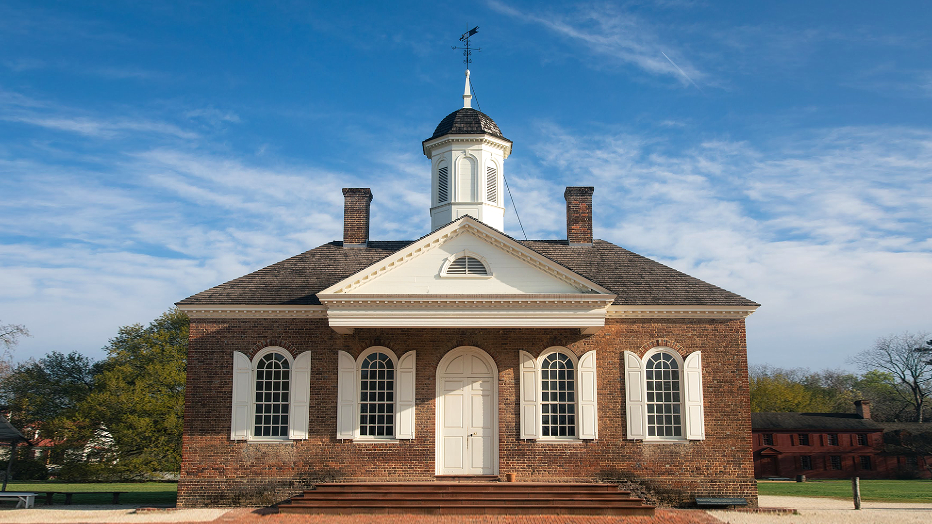 A photograph of the exterior front view of a brick building with white trim, against a blue sky.
