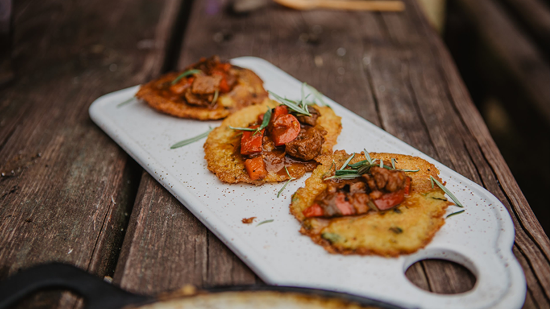 Potato pancakes topped with meat and vegetables served on a white platter on a rustic wooden table.