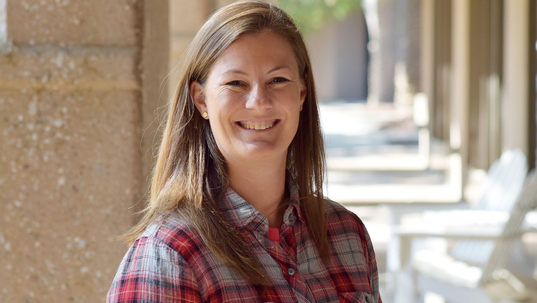 Image shows a woman standing outside on a patio, looking into the camera and smiling.