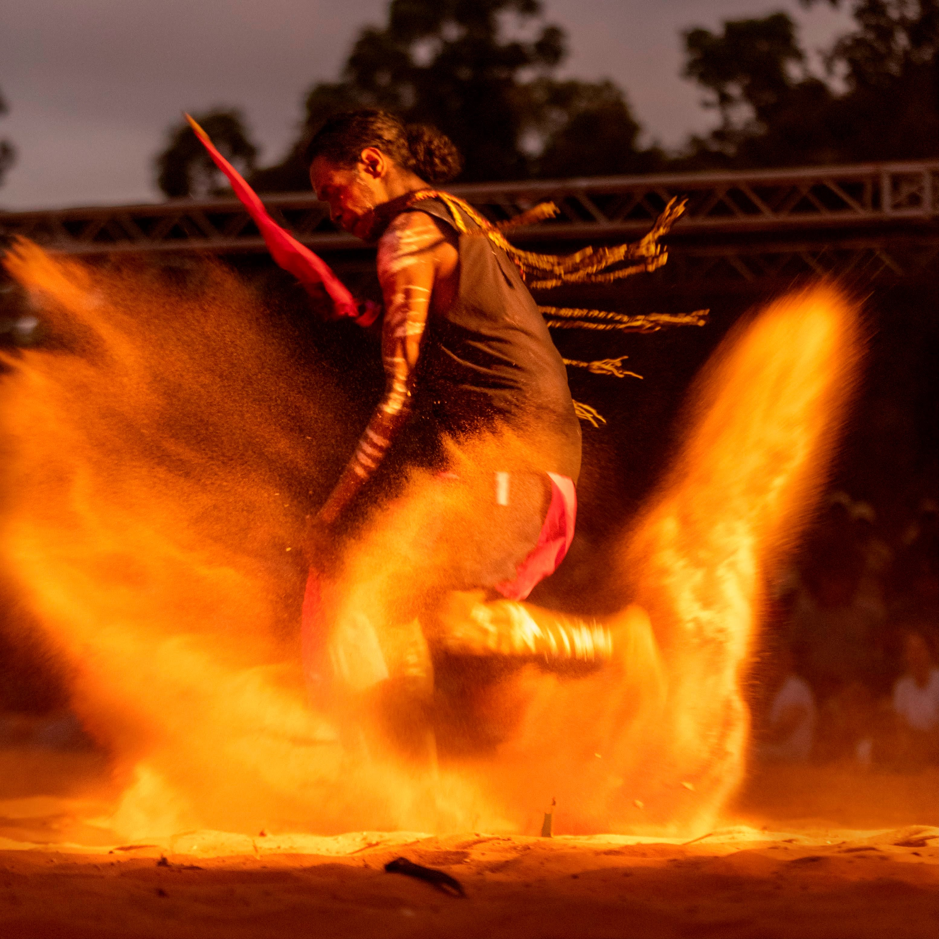 A man dances at Garma Festival at night, kicking up dirt